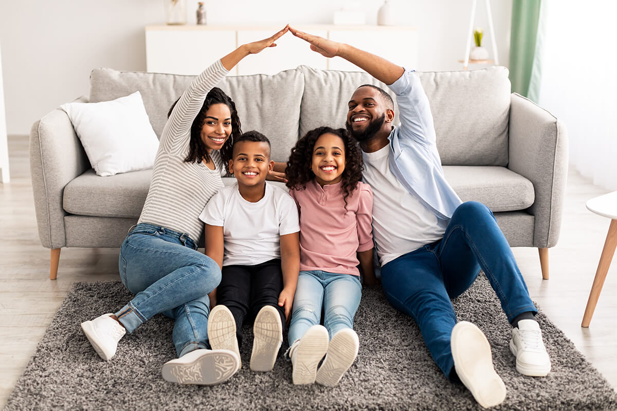 Smiling family sitting together in front of their home, representing the peace of mind that supplemental insurance can provide.